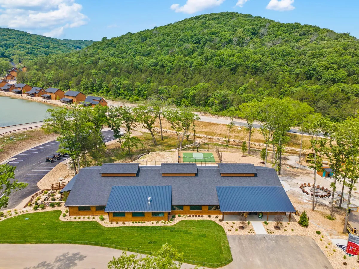 This exterior image features the main building of the resort, with a scenic waterfront, visible basketball court, and a picnic area. The lush landscape and water highlight opportunities for both relaxation and outdoor recreation. There are people enjoying various activities, fostering a lively and family-friendly atmosphere.
