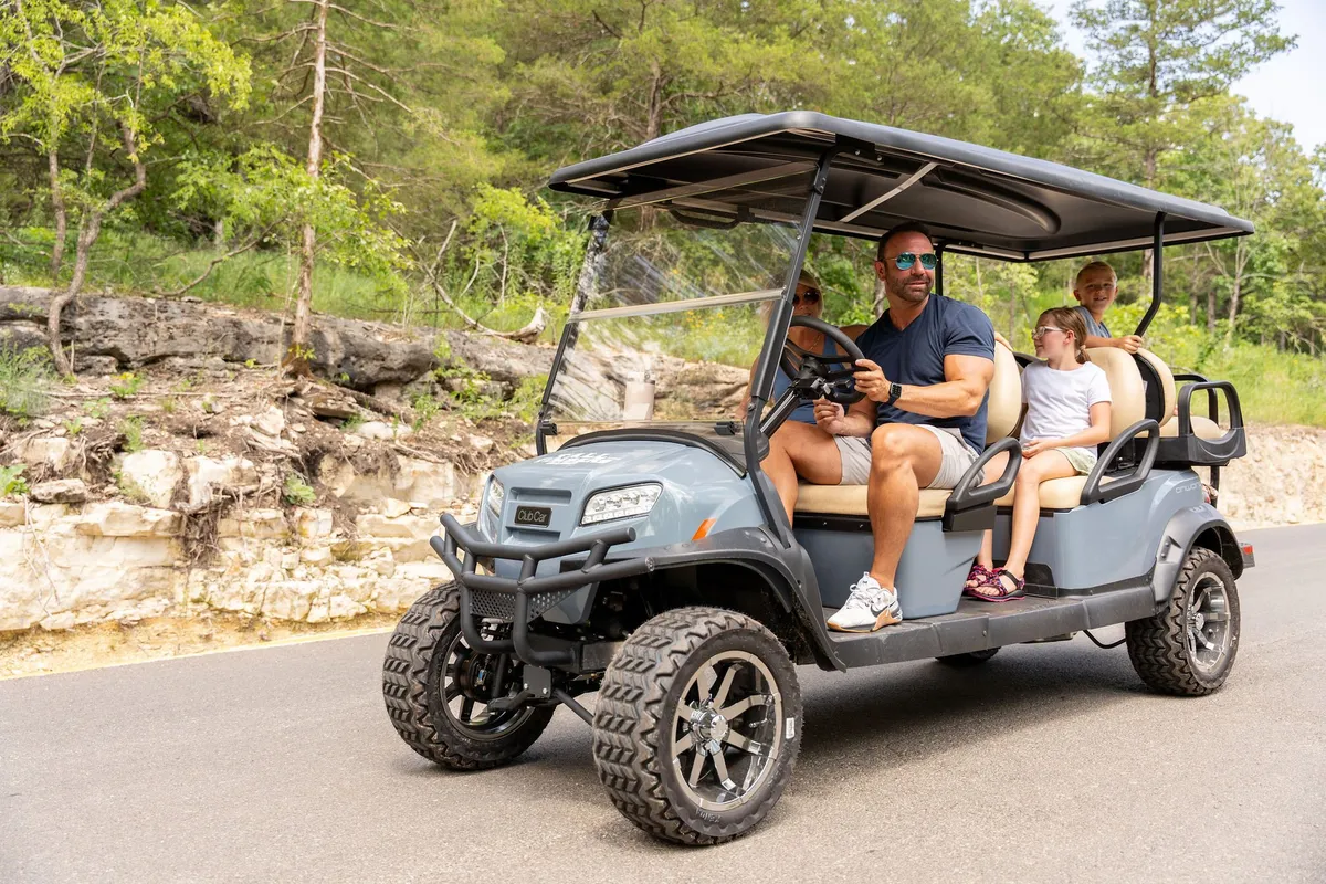 A family rides a golf cart through a natural setting, surrounded by trees and open space. The people are smiling and appear to be exploring or heading to an activity, capturing the playful and adventurous spirit of the resort.