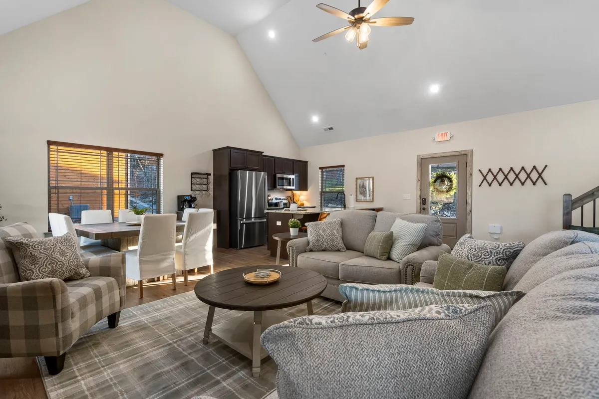 An open-concept interior with comfortable sofas, a dining table, and a visible kitchen area. Large windows flood the space with natural light, enhancing the warm and inviting mood.