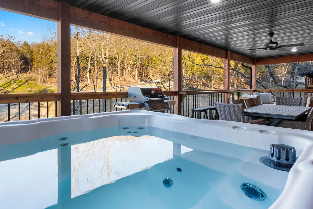 An outdoor deck with a dining area, grill, hot tub, and scenic landscape views. The setting is tranquil, perfect for al fresco dining, grilling, or enjoying morning coffee while surrounded by nature.