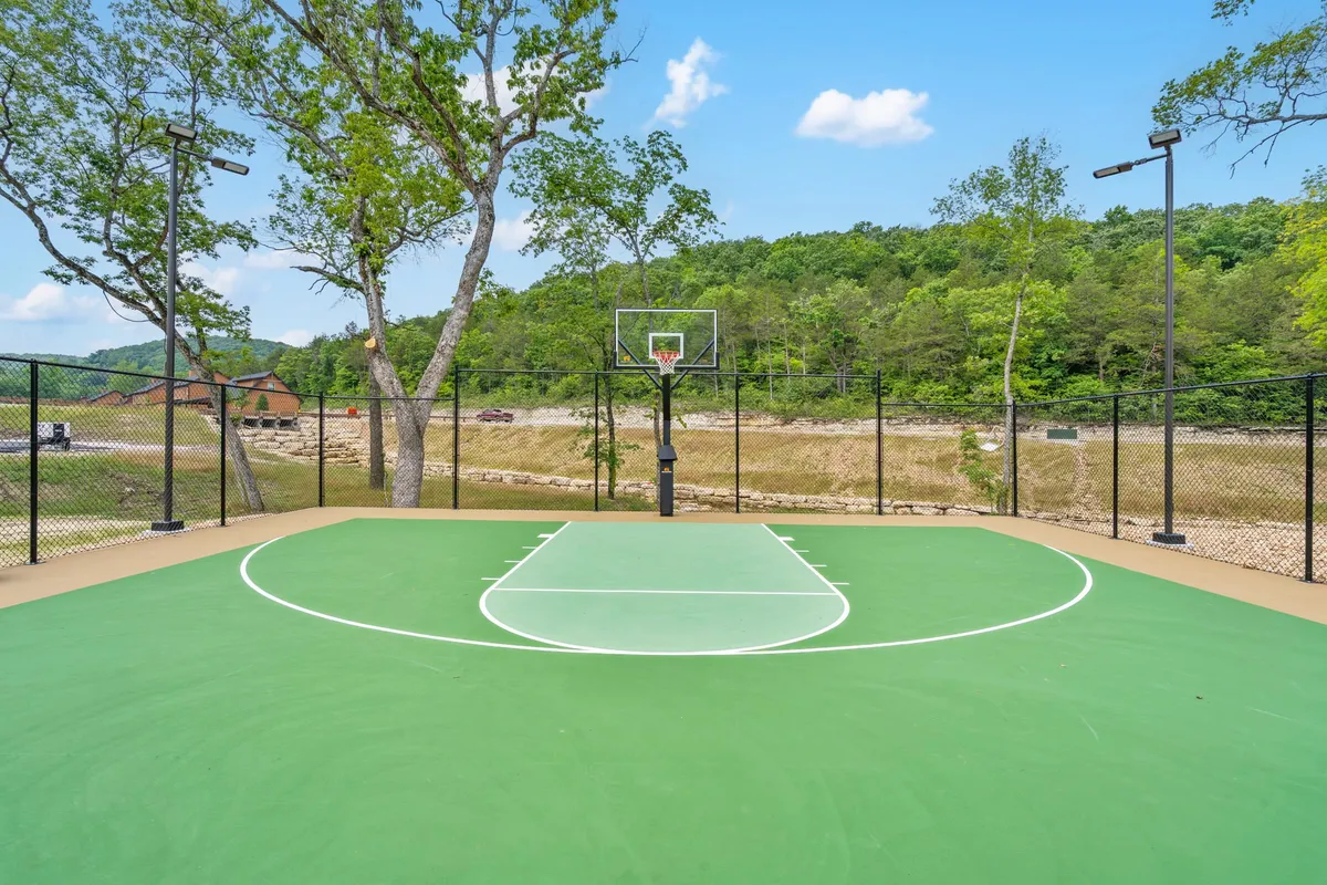 An exterior view of a vibrant basketball court surrounded by trees, with a hoop and green playing surface. The setting is energetic, inviting guests to participate in friendly games and enjoy the outdoors.