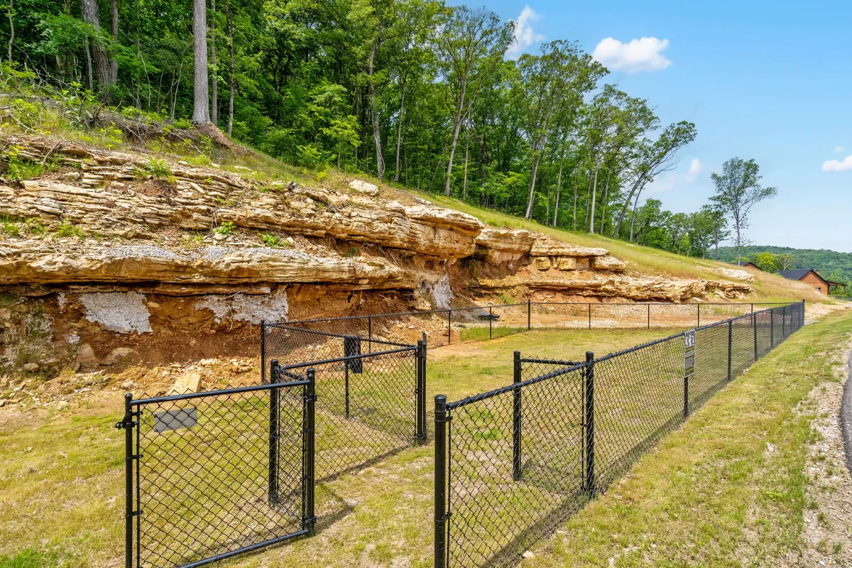A tranquil natural setting featuring a striking rock formation within a fenced area, surrounded by lush trees and open skies, with soft sunset light enhancing the peaceful mood. The landscape evokes adventure and relaxation in nature, inviting guests to explore nearby trails and scenic beauty.