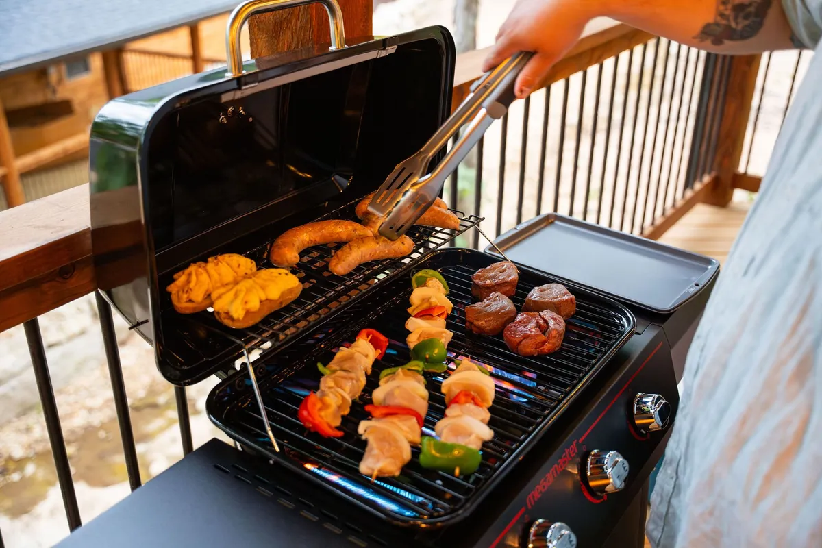 A close-up of an outdoor grill in action, with hands using tongs to cook food. The lively scene captures the joy of barbecuing and socializing outdoors.