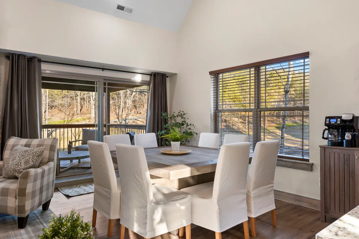 A cozy dining area with a large table, comfortable chairs, expansive windows bringing in natural light, and a quaint coffee station. The space feels perfect for family dinners, morning coffees, or board game nights.