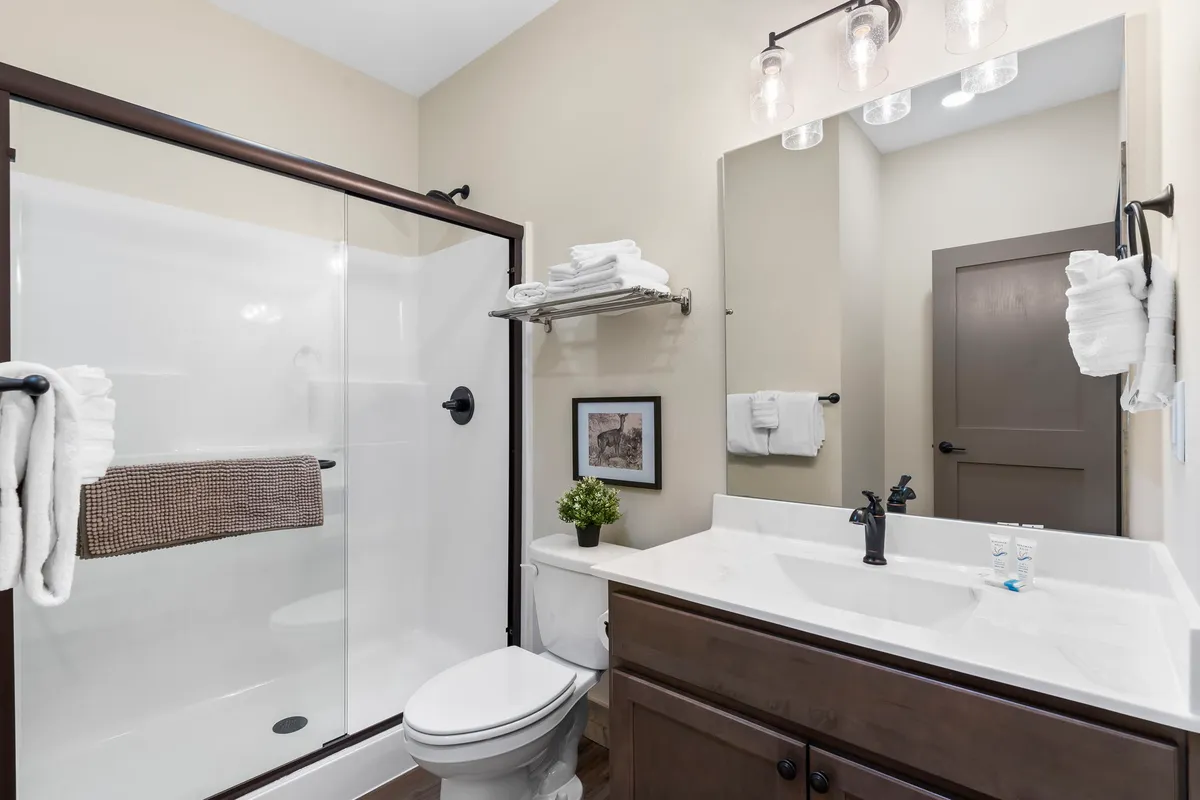 A modern ensuite bathroom with a glass shower enclosure, elegant dark wood vanity, framed artwork, and a decorative plant. The space feels refreshing and private, perfect for self-care and relaxation.
