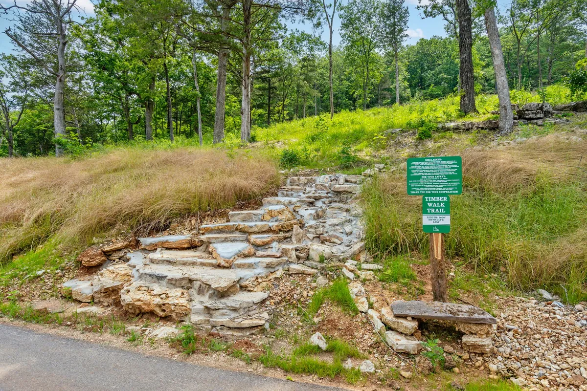 A stone pathway bordered by lush greenery leads to a trail sign, inviting guests to embark on a hike or nature walk. The scene captures a sense of adventure and discovery, encouraging outdoor exploration for visitors and their pets alike.